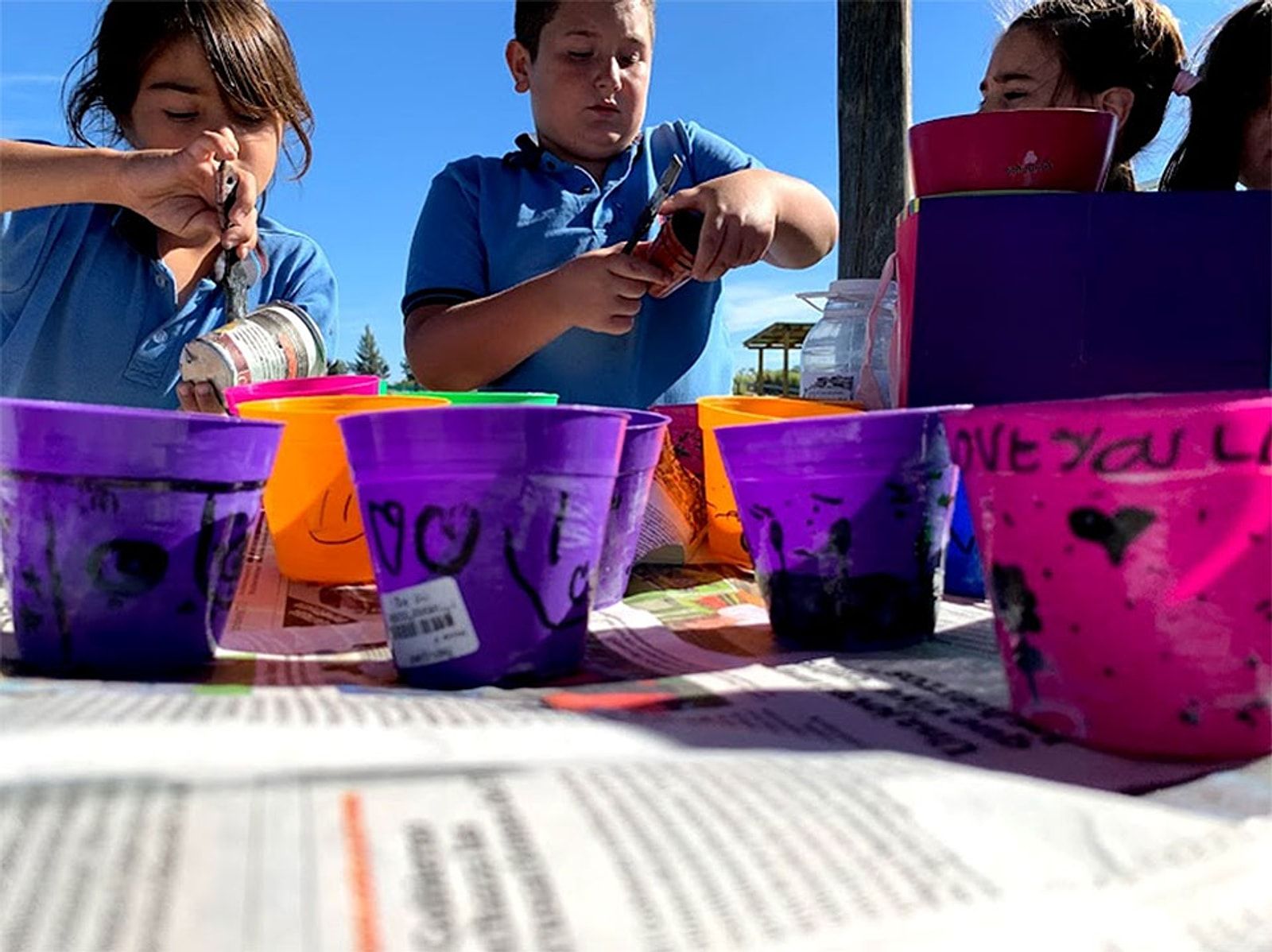 Alumnos decorando macetas de colores al aire libre para la huerta